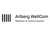 Das Arlberg WellCom Logo zeigt schwarze Schrift auf weißem Hintergrund mit senkrechten Streifen. Es steht für Wellness, Kommunikation und Veranstaltungsräume.